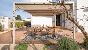 Un espace extérieur abrité, aménagé pour les repas, avec une table et des chaises, entouré de plantes et d’une pergola.
