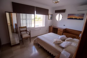Quarto com cama, cadeira, cômoda, espelho e janela com persianas.