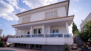 A two-story building with a balcony, a swimming pool, and potted plants.