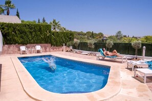 Ein Pool mit gewölbter Kante, Liegestühlen und wolkenlosem, blauem Himmel.