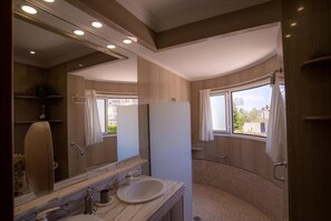 Ein Badezimmer mit Marmorwaschtisch, Spiegel, Dusche und einem Fenster mit Vorhängen.