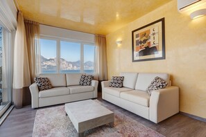 Un salon avec deux canapés, une table basse, une grande fenêtre avec des rideaux, un luminaire fixé au mur et un tableau encadré.