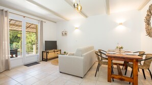 Ein Wohnzimmer mit einer Couch, einem Esstisch, Stühlen, einem Fernseher und einem Balkon mit Vorhängen.