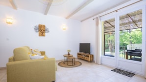 Una sala de estar con sofá, televisor, una mesita con un florero y un ventanal corredizo hacia el exterior.
