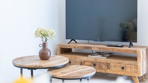 Un mueble de televisión de madera con un televisor de pantalla plana, un florero con flores y dos mesas redondas.