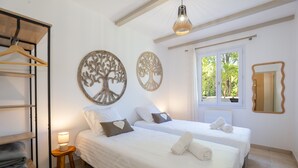 Camera da letto con due letti, un armadio in legno, un tavolino con una lampada e decorazioni murali a tema alberi.