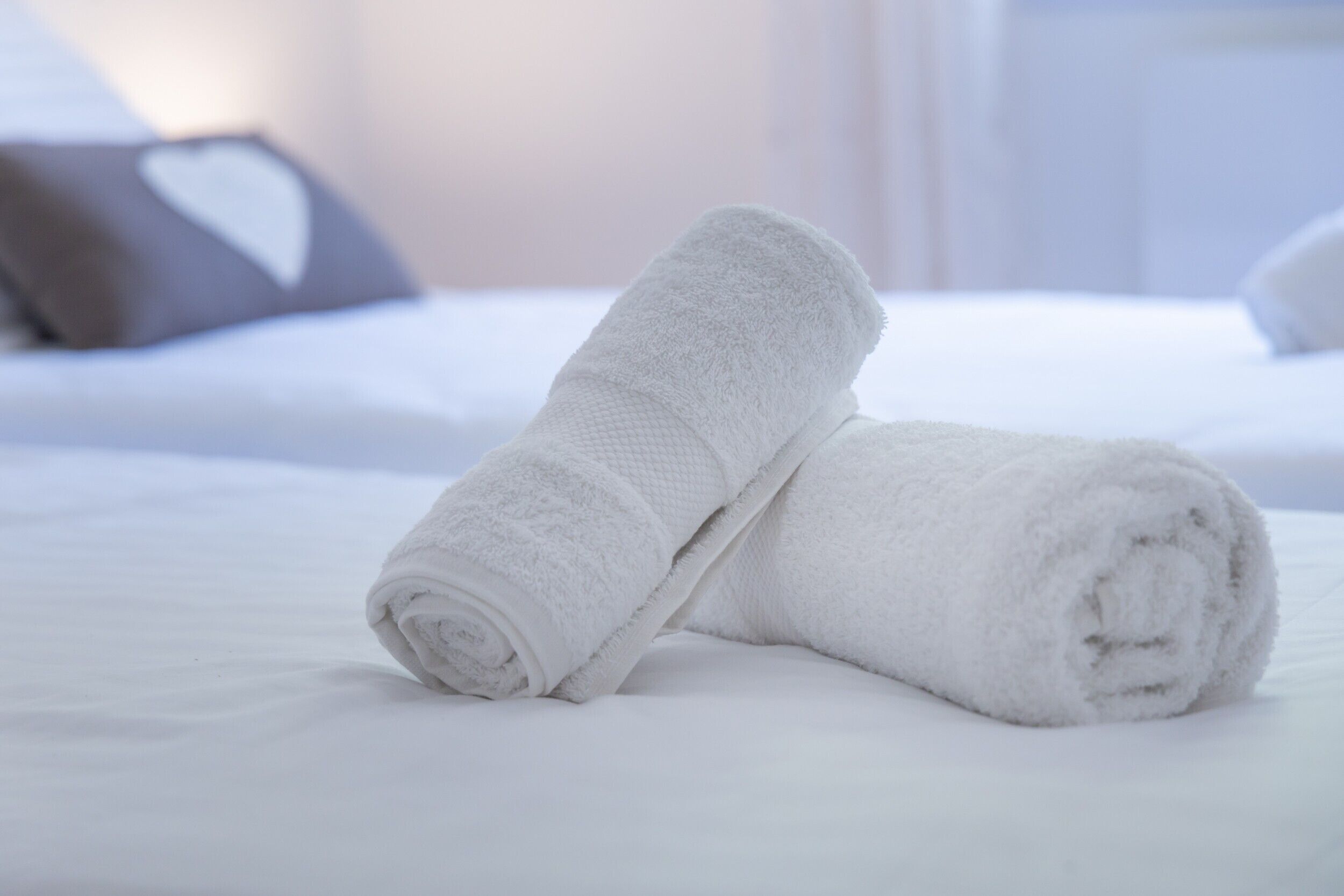 Ein ordentlich bezogenes Bett mit weißer Bettwäsche und zwei aufgerollten weißen Handtüchern.