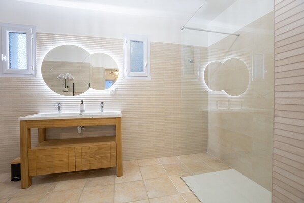 A modern bathroom with a wooden vanity, a large mirror, and a glass shower enclosure.