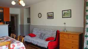 A cozy room with a sofa, a wooden dresser, a dining table, and a kitchen area.