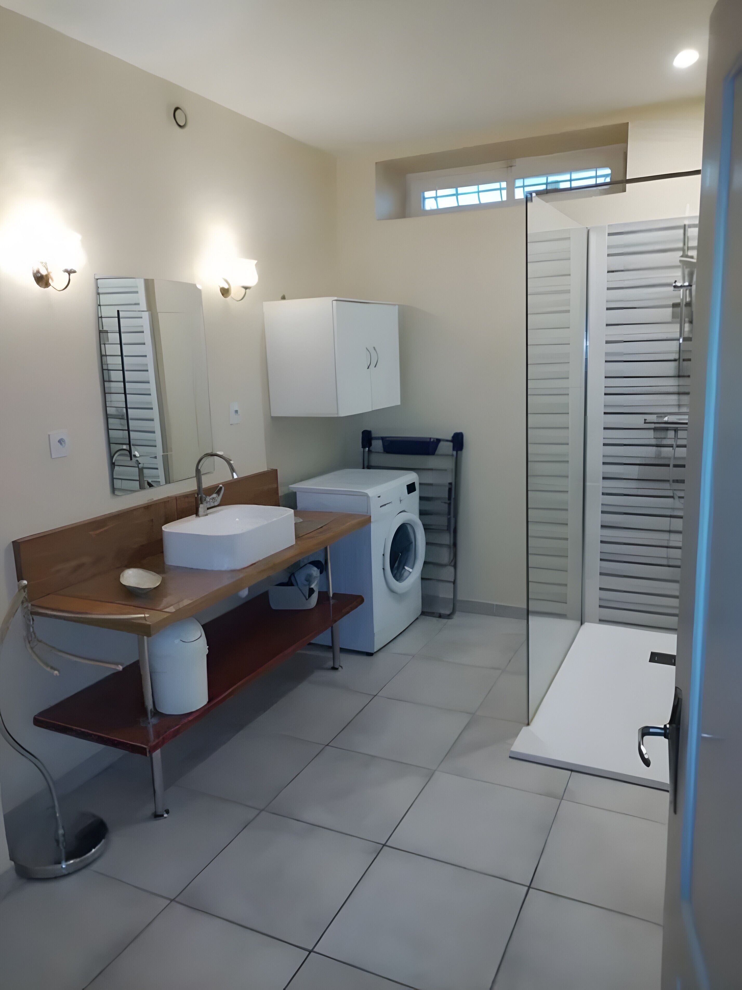 A modern bathroom with a sink, mirror, cabinet, washing machine, and a shower area.
