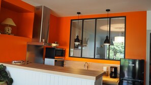 Eine Küche mit orangefarbenen Wänden, einer Edelstahl-Dunstabzugshaube, einer Mikrowelle, einer Kaffeemaschine und einem Kühlschrank.