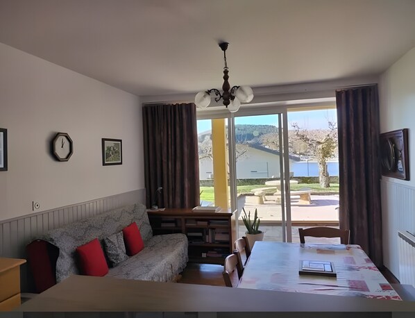 A room with a sofa, a dining table, a chandelier, a clock, and a view of a lake.