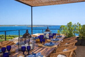 Un espace de restauration en plein air offrant une vue sur la mer, avec des meubles en osier et de la vaisselle en verre bleue.