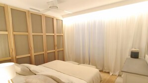 Un dormitori amb llit, escriptori, cadira, armari i finestra amb cortines.
