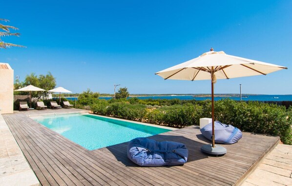 A poolside area with lounge chairs, umbrellas, and a view of the sea.
