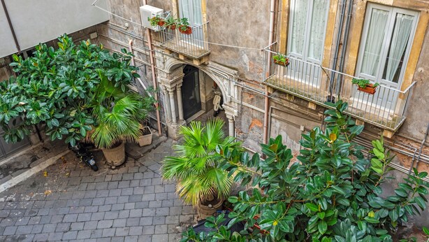 A courtyard with potted plants, a brick floor, and a building with a balcony. - Room 'Angelica' with Wi-Fi and Air Conditioning (Catania)
