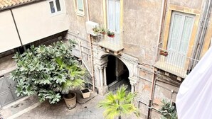 A courtyard with potted plants, a motorcycle, and a building with a balcony. - Room 'Angelica' with Wi-Fi and Air Conditioning (Catania)