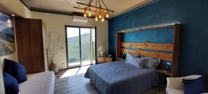 Une chambre à coucher avec un grand lit, une tête de lit en bois, une table de chevet, une lampe et une vue sur l’extérieur.