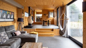 Un intérieur moderne avec un plafond en bois, un canapé, une table, un fauteuil suspendu et une vue dégagée grâce à de grandes fenêtres.