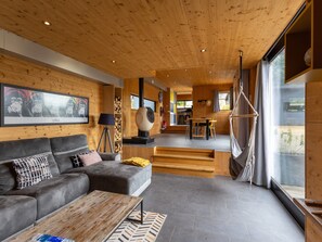 Ein modernes Interieur mit Holzboden, einem grauen Sofa, einem Holztisch und einem großen Fenster.