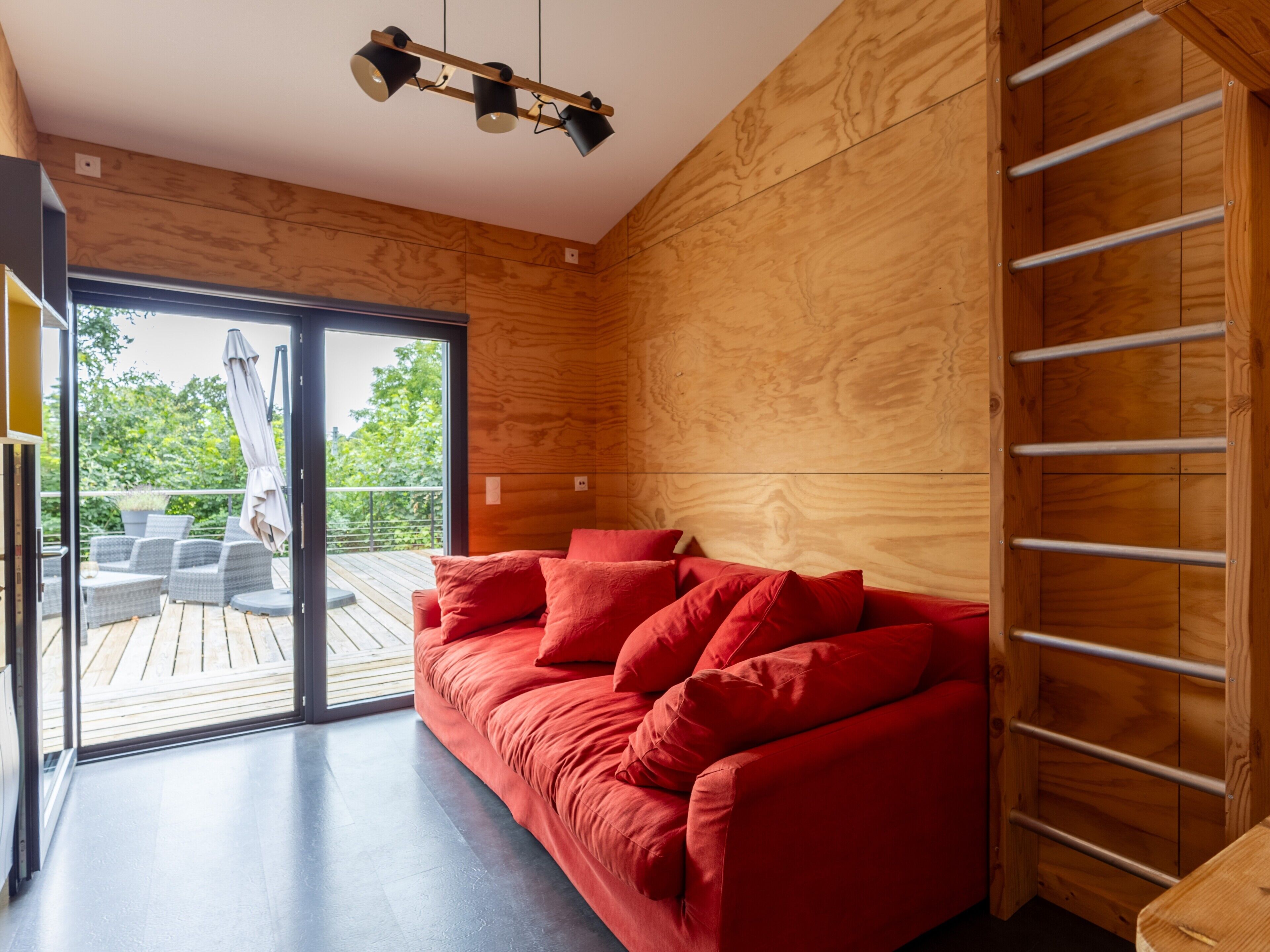 A modern interior with a wooden wall, a red sofa, and a sliding glass door leading to an outdoor deck.