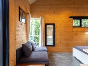 Ein Holzblockhaus-Innenraum mit einer Couch, einem Bett und einem Fenster mit Vorhängen.