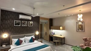 A modern hotel room with a bed, desk, and chair, featuring a dark textured wall, ceiling fan, and artwork. - Pride Elite Dwarka (Dwarka)