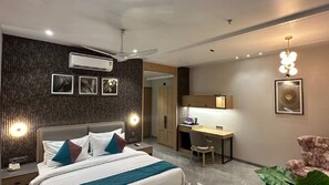Moderni hotellihuone, jossa on sänky, työpöytä ja tuoli. Huoneessa on tumma, kuvioitu seinä, kattotuuletin ja taideteoksia.