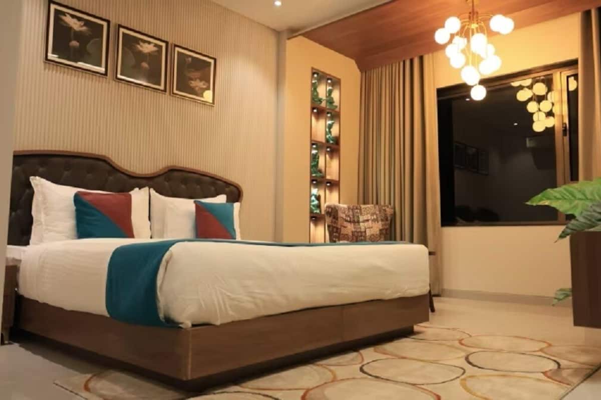 A neatly made bed with a wooden headboard, a decorative wall panel, and a hanging light fixture.