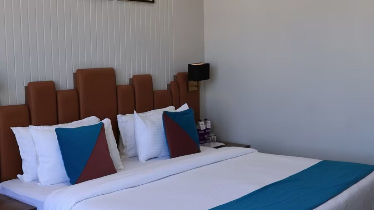 A hotel room with a bed, pillows, a nightstand, and a lamp.