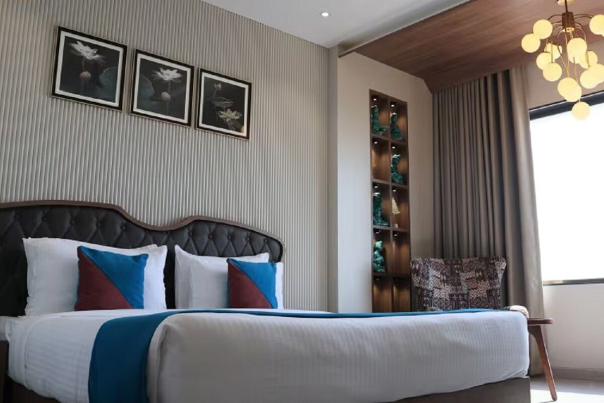 Ein modernes Hotelzimmer mit einem großen Bett, einem Nachttisch, einem Sessel, einem Bücherregal und einem großen Fenster mit Vorhängen.