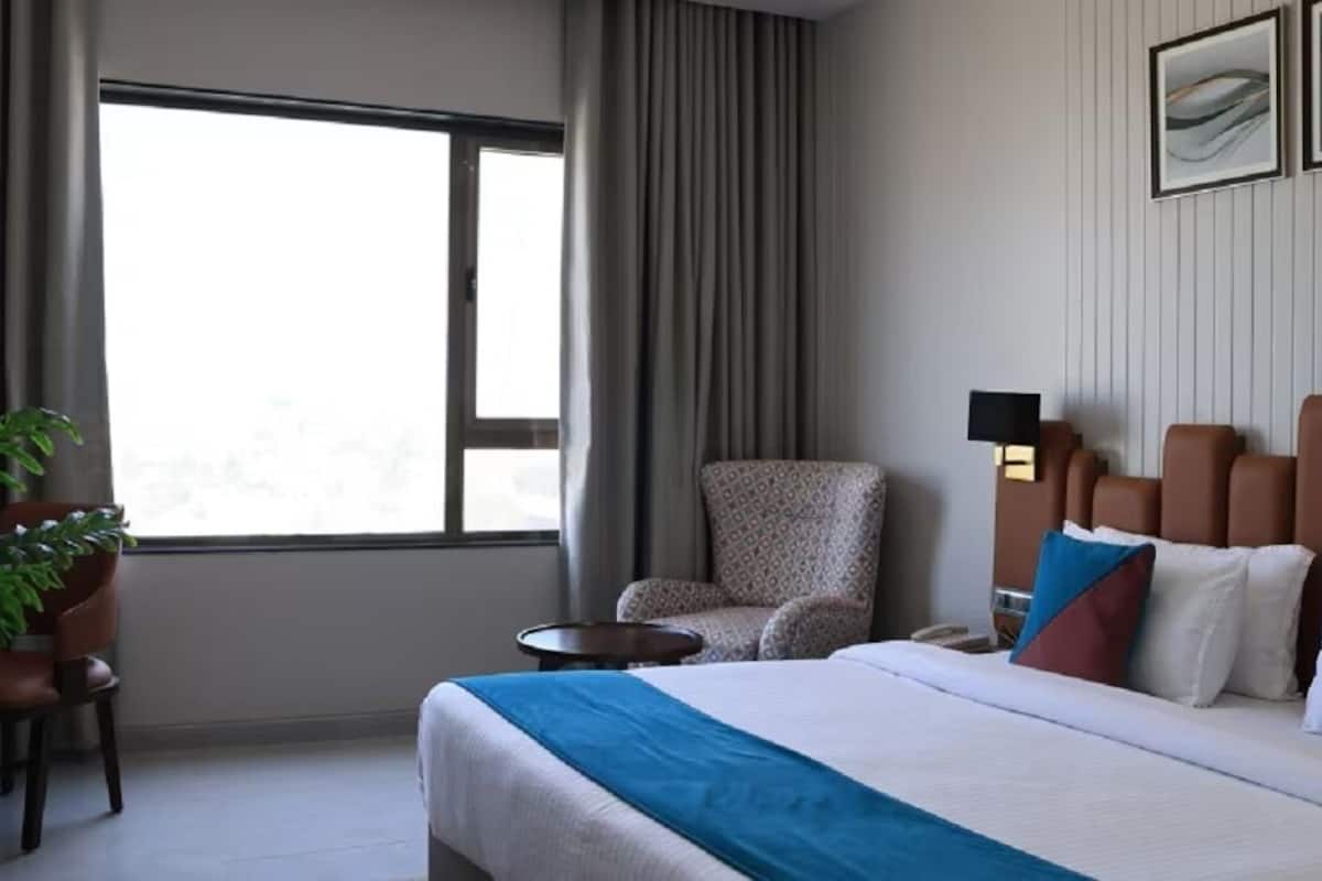 A hotel room with a large bed, a chair, a small table, and a potted plant.