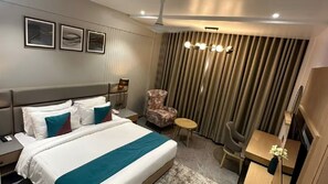 Hotellihuone, jossa on sänky, tuoli, työpöytä ja verho.