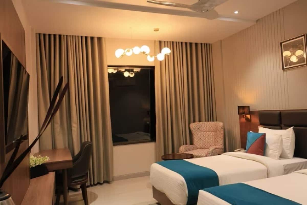 A hotel room with two beds, a desk, a chair, and a large window with curtains.
