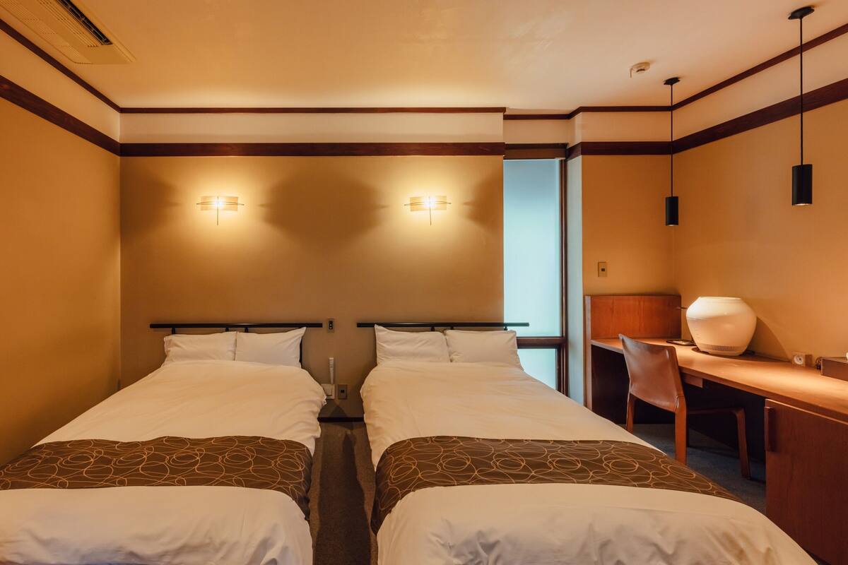 A hotel room with two beds, a desk, and a chair.