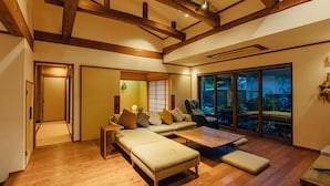 A spacious living room with a sofa set, a coffee table, and a view of a garden through large glass doors. - Fukahoritei (Kurume)