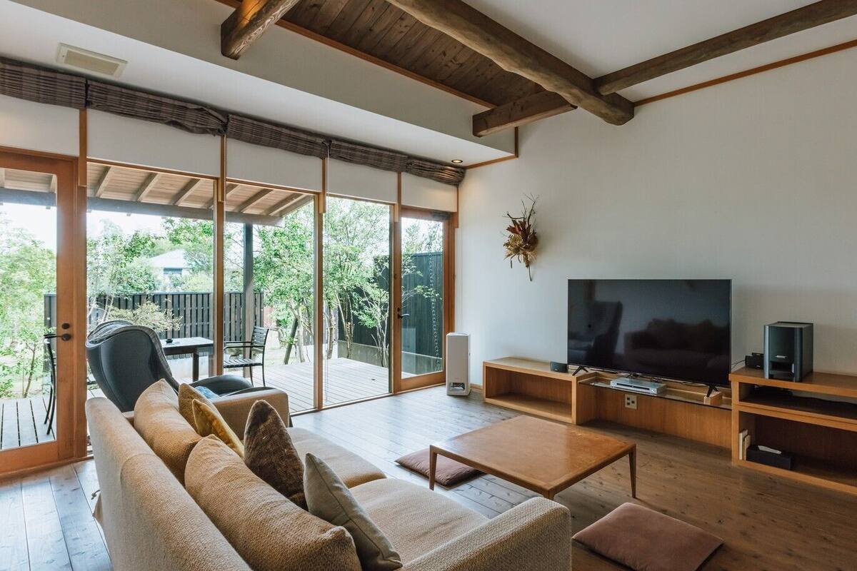A modern living room with a large TV, wooden furniture, and a sliding glass door leading to an outdoor area.