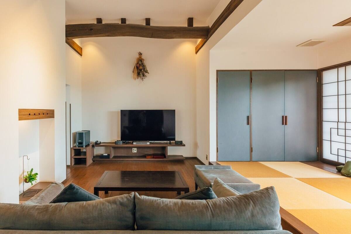 A modern living room with a TV, sofa, and wooden beams on the ceiling.