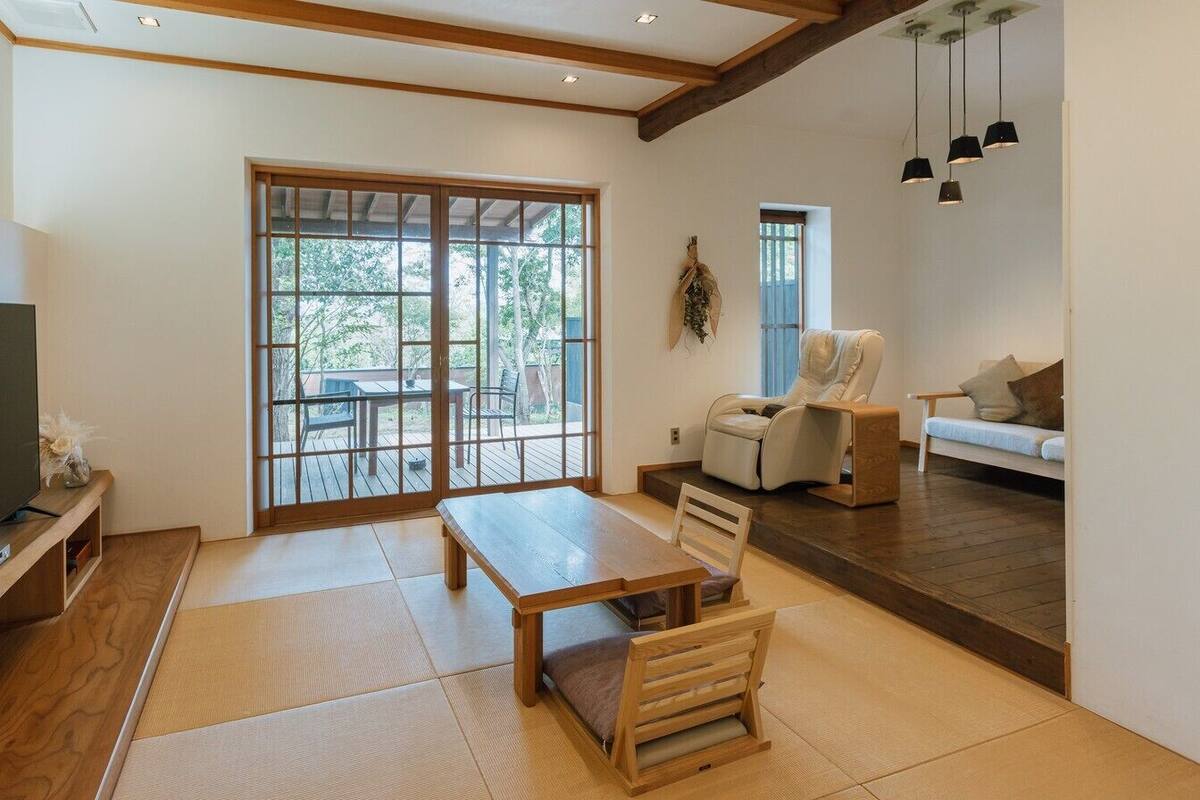 A living room with tatami flooring, a television, a sofa, and a sliding glass door leading to an outdoor deck.