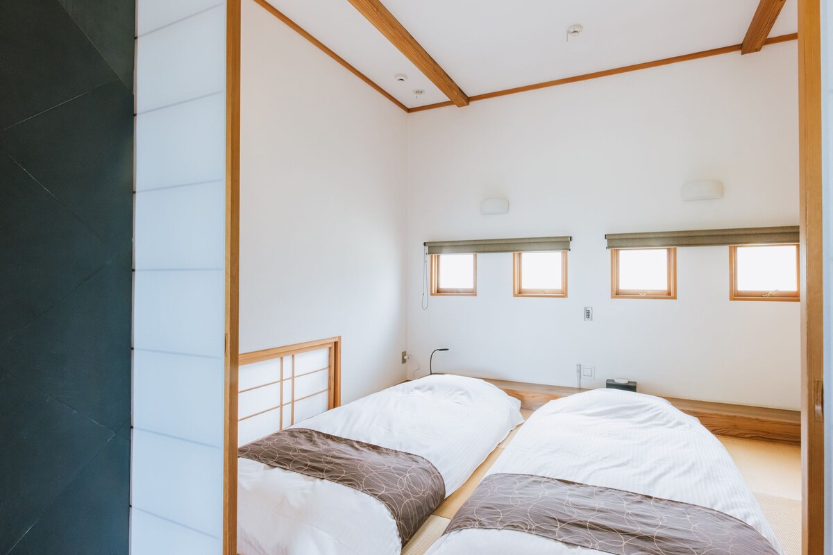 A minimalist room with two beds, a window, and a wooden ceiling structure.