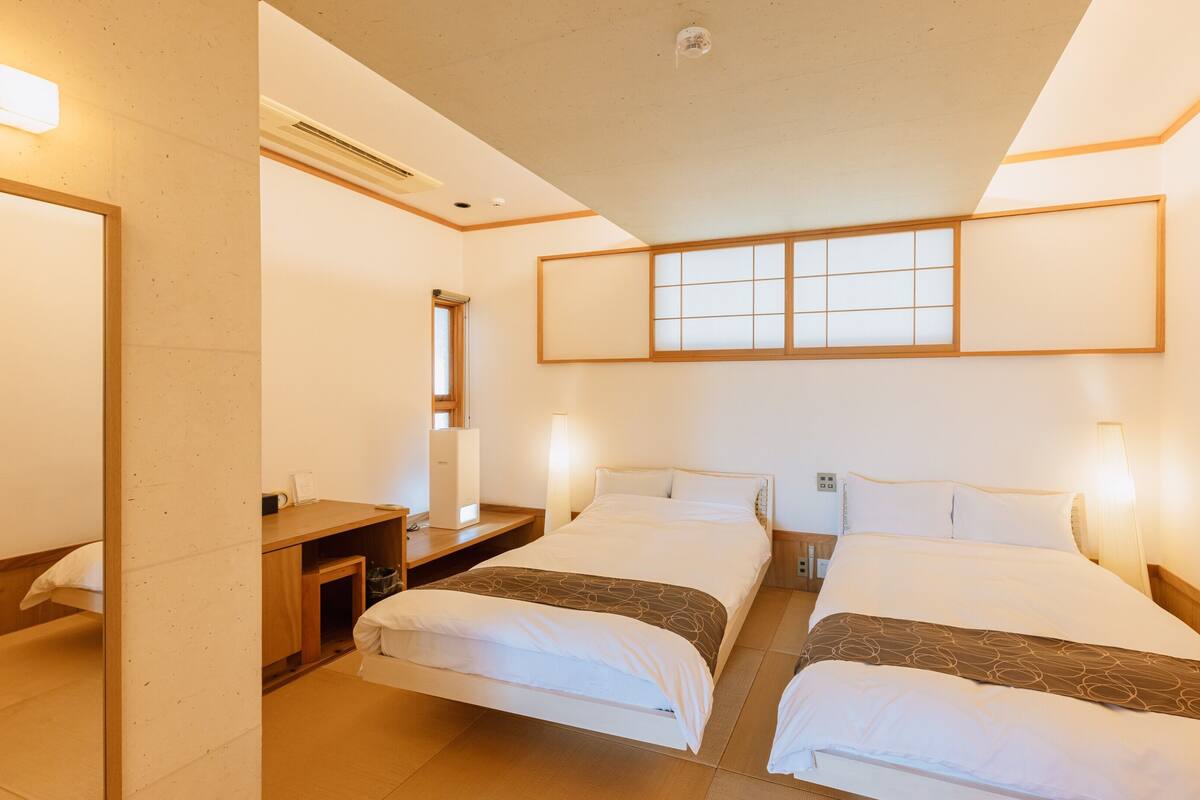 A hotel room with two beds, a desk, a mirror, and a window with a view.