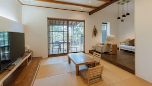 A living room with a TV, a sofa, a recliner, a table, and a sliding door to a patio. - Fukahoritei (Kurume)
