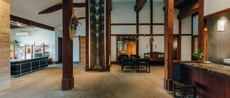 A spacious interior with high ceilings, exposed wooden beams, a central column, and a reception area with a counter and seating.