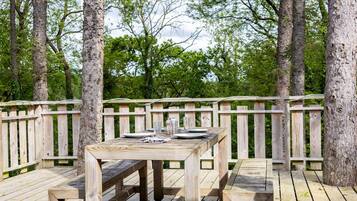 Une terrasse en bois avec une table et des bancs, entourée d’arbres.