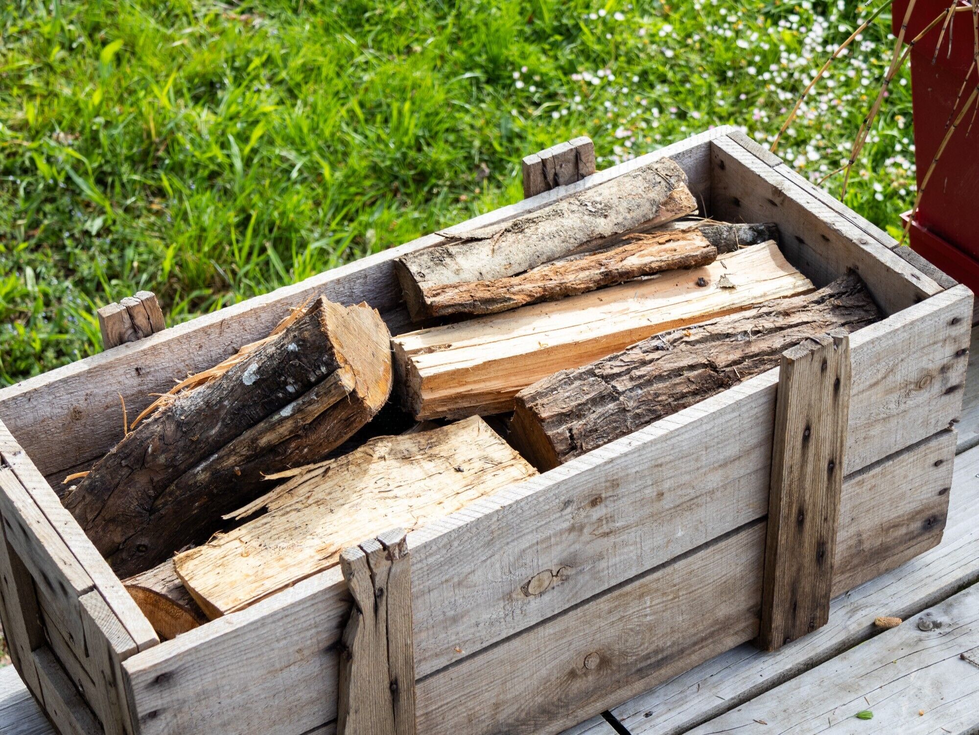 A wooden crate filled with logs, placed outdoors on a grassy area.