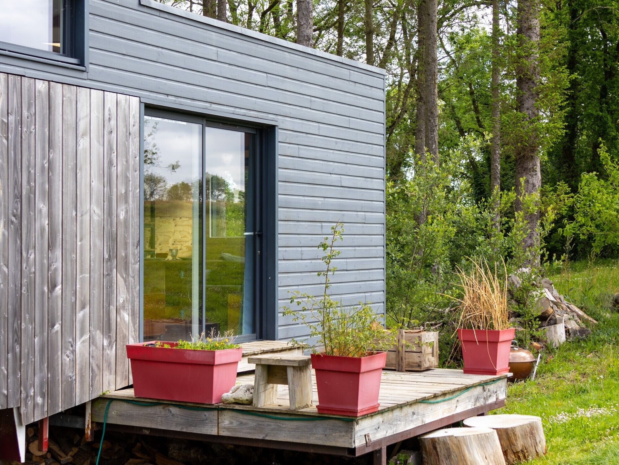 Ein modernes Haus mit großen Schiebeglastüren, einer Holzterrasse und Topfpflanzen.