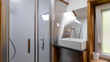 Un baño moderno con cabina de ducha de vidrio, un lavabo blanco y un marco de ventana de madera.
