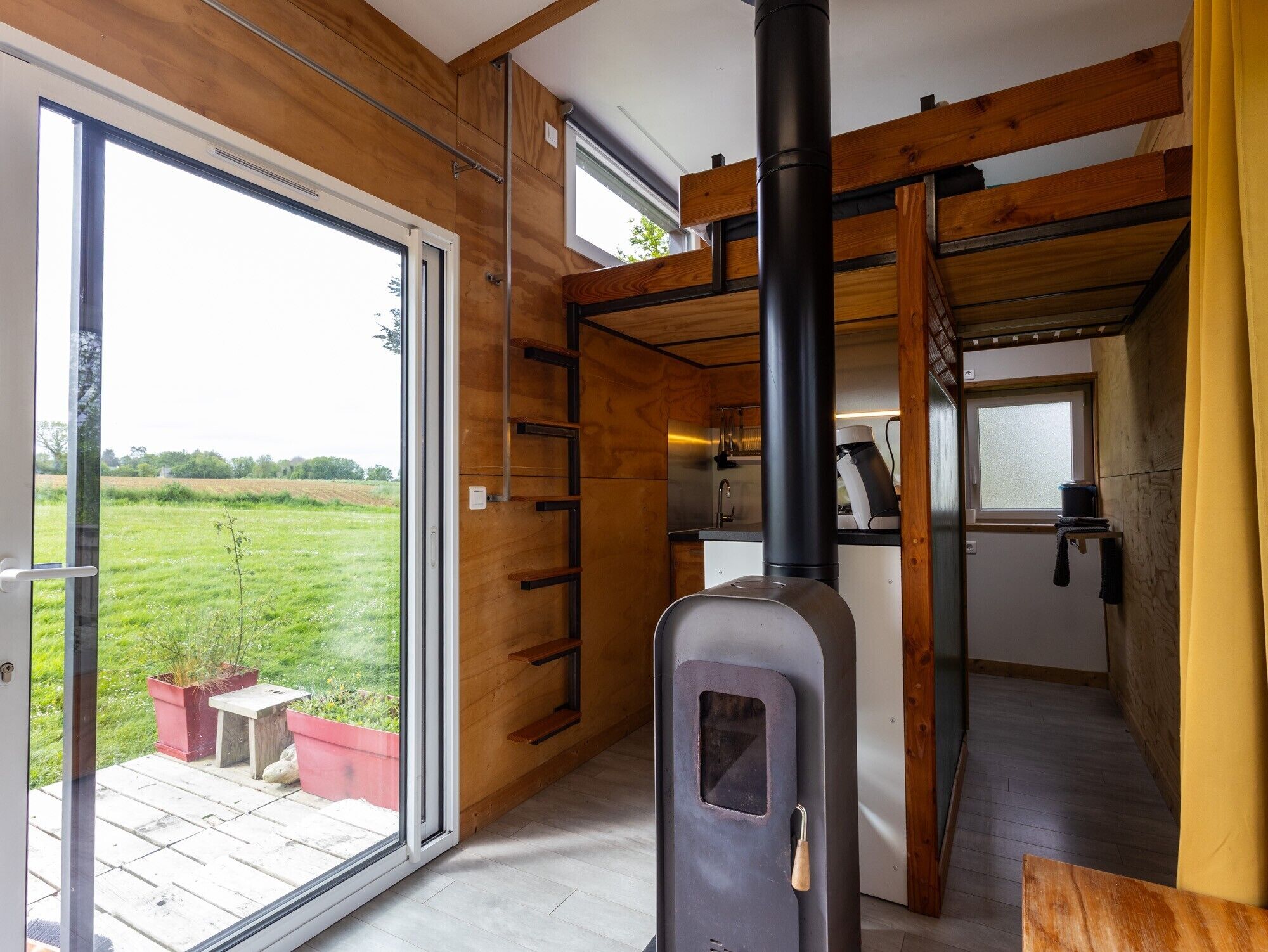 Un interior moderno con una habitación revestida de madera, una estufa negra y vistas a un campo verde a través de un ventanal.