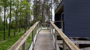 A wooden deck leading to a dark-colored cabin in a forested area.