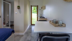 A modern room with a bed, a dining table, a kitchen area, and a bathroom. - Chalet 'La Cafoutche De Minus Renovated' with Private Terrace, Shared Garden & Wi-Fi (Gommenec'h)